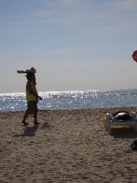 Ein Strandverkaeufer trägt seine Waren auf dem Kopf